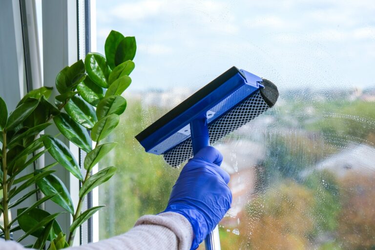 Employee hand in rubber protective glove cleans window with foam and puller. General spring cleaning